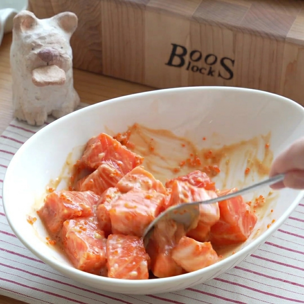 A close-up of seasoned salmon cubes being gently tossed in a mixing bowl.