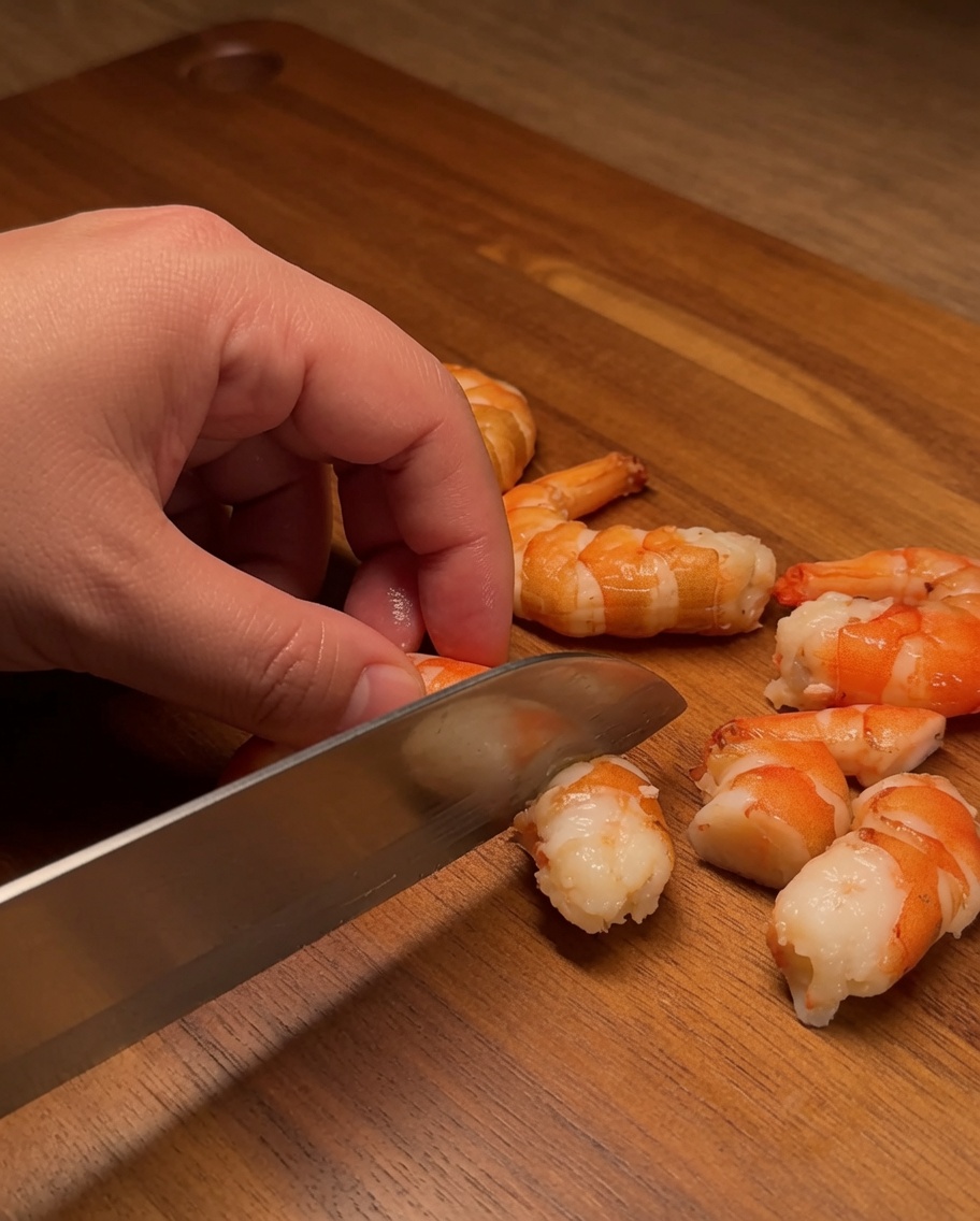 Raw salmon fillet being cut into neat, uniform cubes on a wooden board.