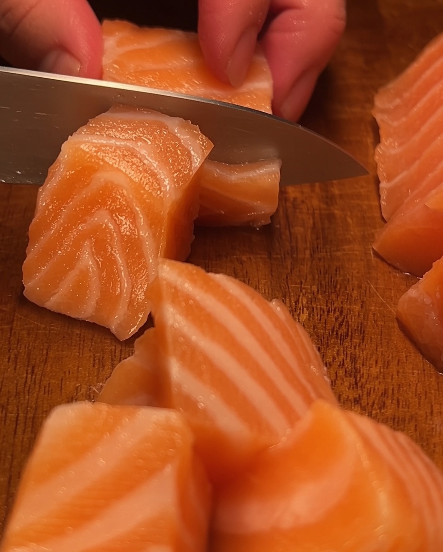 A piece of grilled eel being cut into small, appetizing segments on a wooden cutting board.