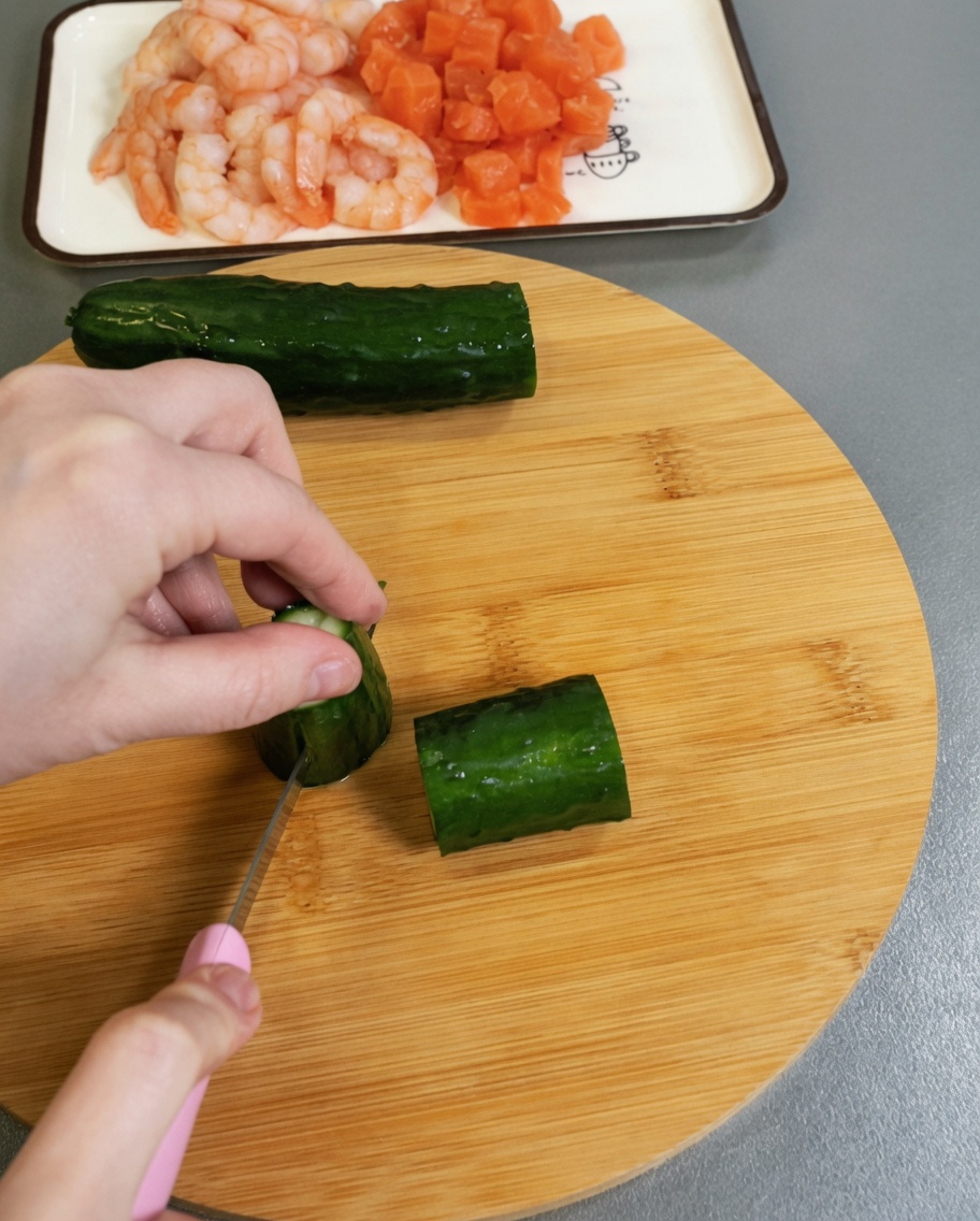 Fresh green cucumber being chopped into small cubes on a wooden surface.