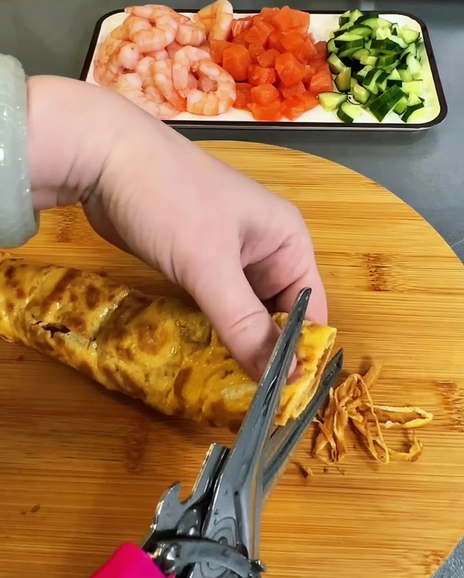 Cooked egg omelet being carefully snipped into thin strips with kitchen scissors.