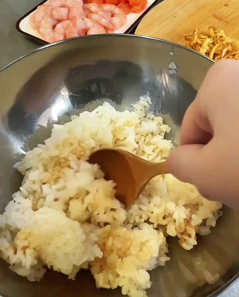 Cooked rice being seasoned with vinegar and soy sauce in a metal mixing bowl.