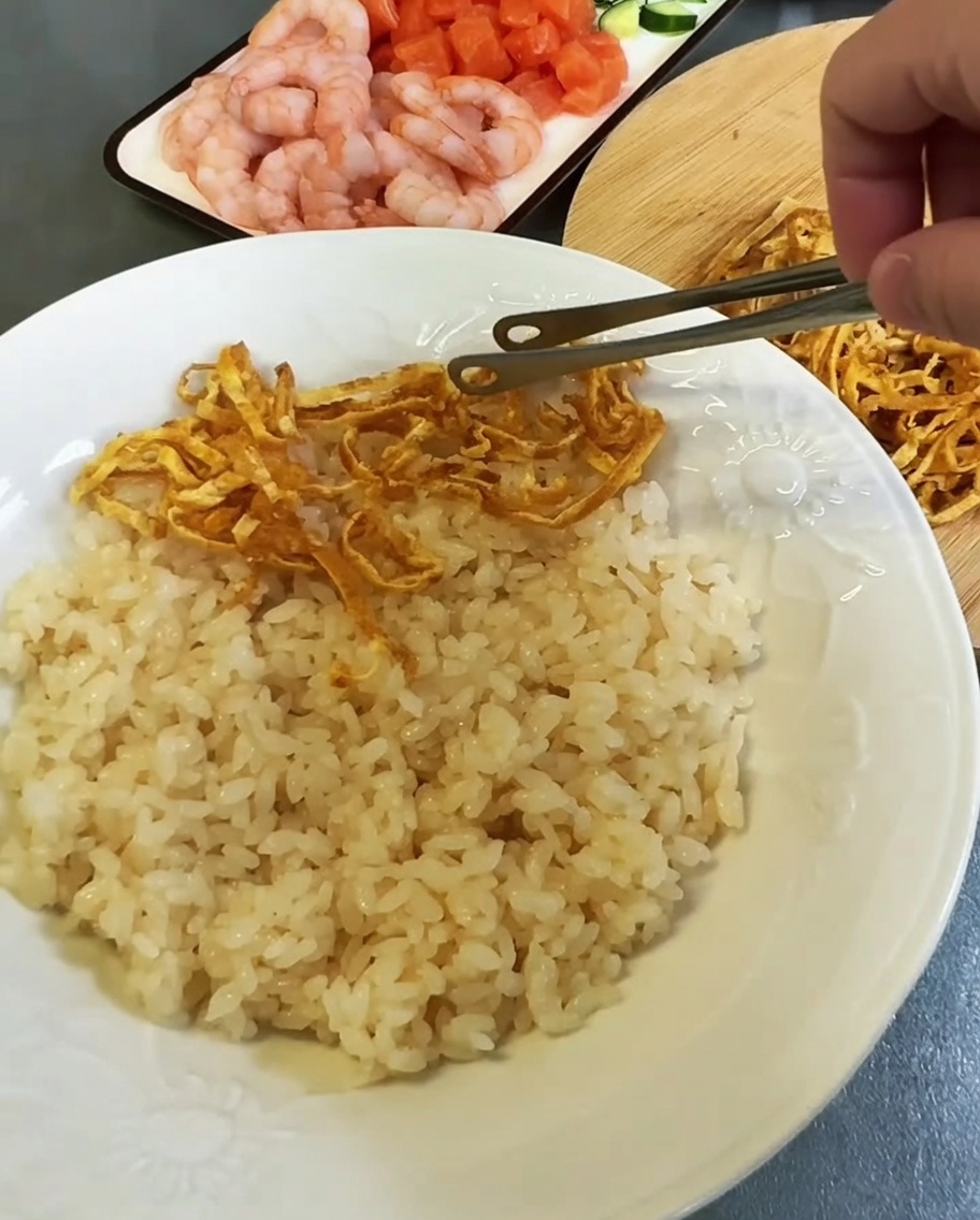 Arranging colorful egg strips and seafood toppings over a bed of seasoned rice on a white plate.