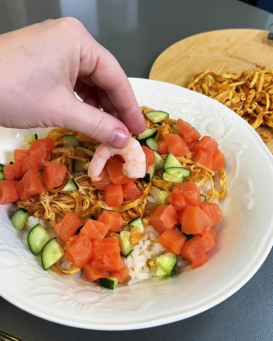 Clusters of fresh diced raw salmon being placed onto the prepared rice plate.