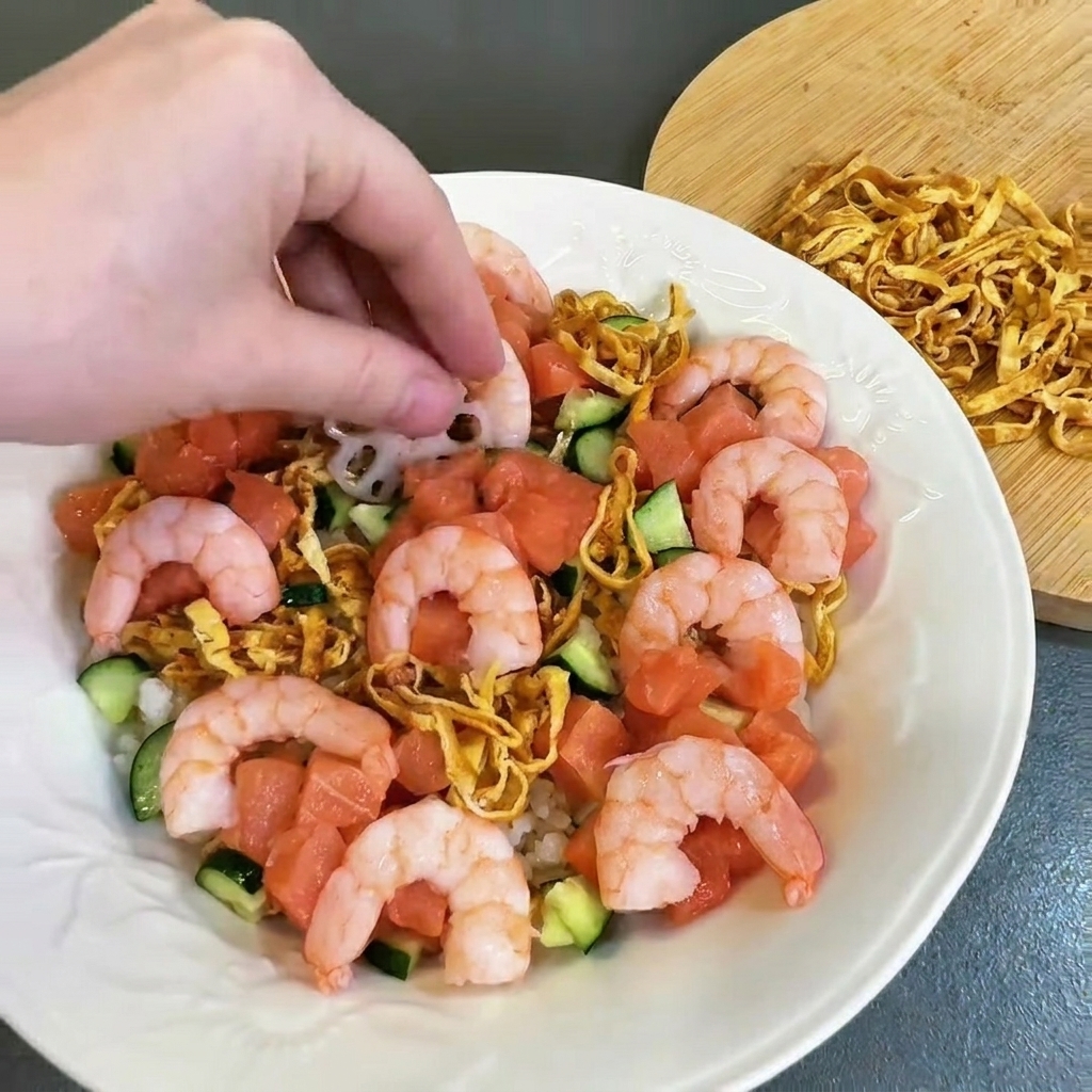 Cooked pink shrimp being arranged carefully onto the plate filled with salmon and cucumber.