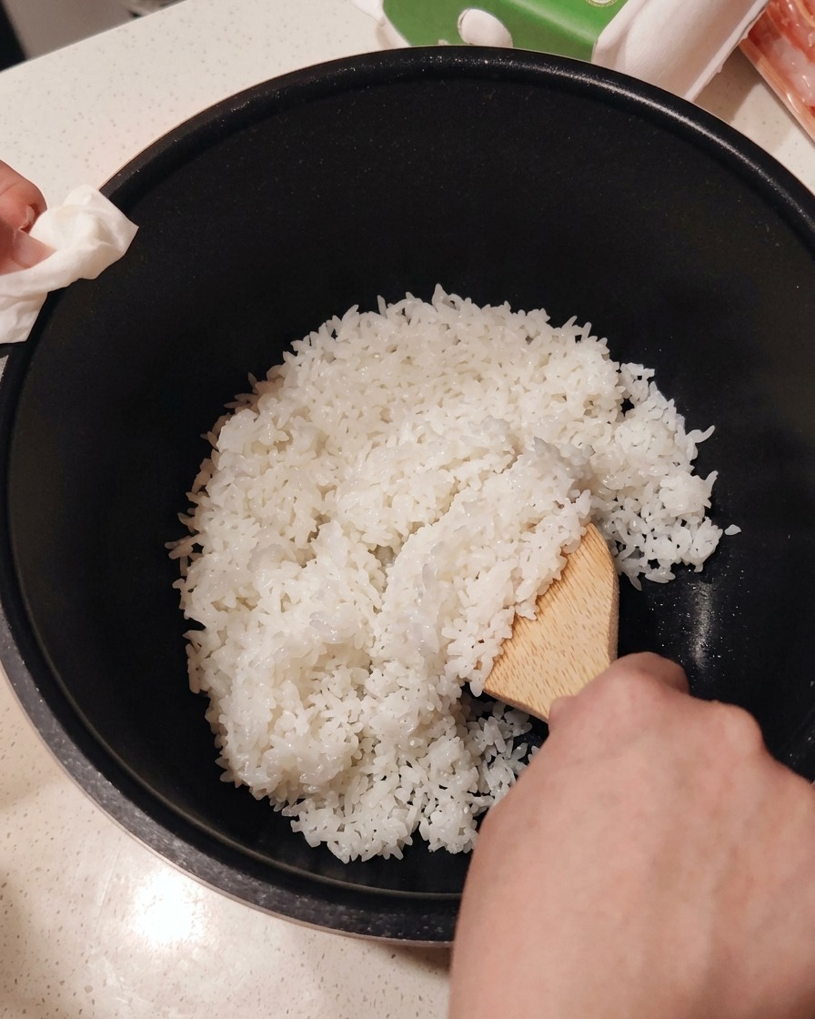 Mixing sushi vinegar into freshly cooked white rice in a bowl using a wooden paddle.