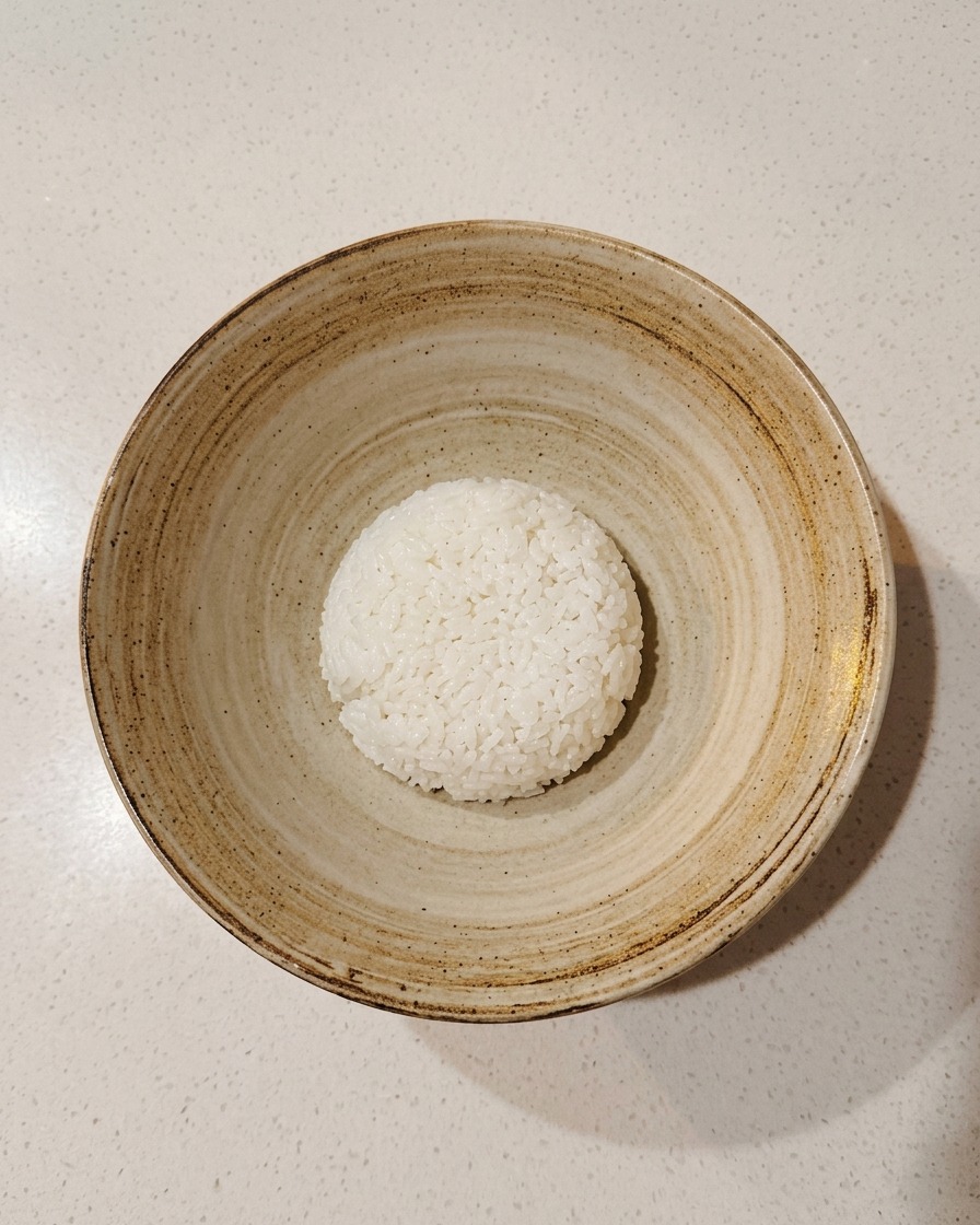 A single scoop of seasoned sushi rice centered in an empty, rustic ceramic serving bowl.