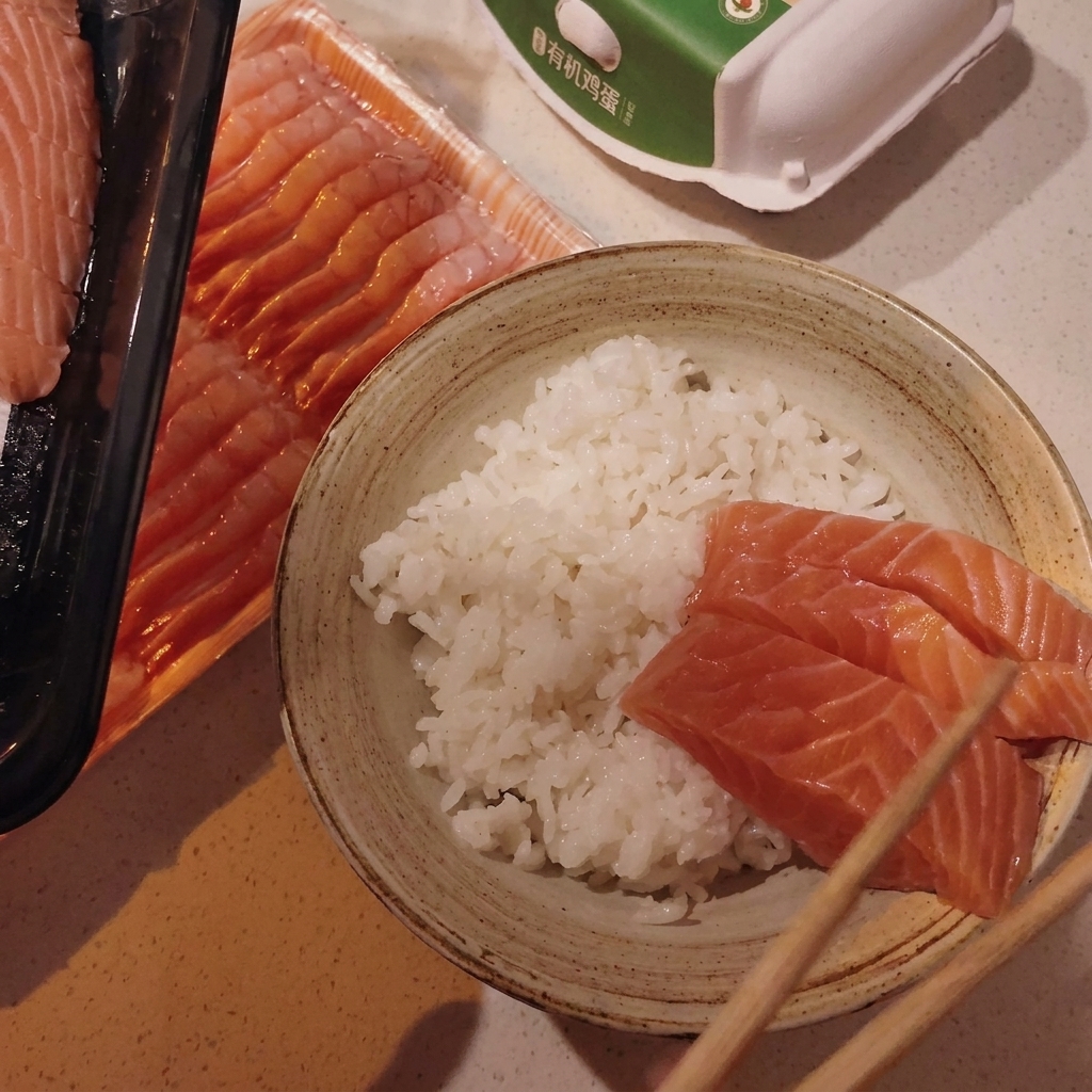 Arranging raw salmon and raw scallop slices over rice in a serving bowl with chopsticks.