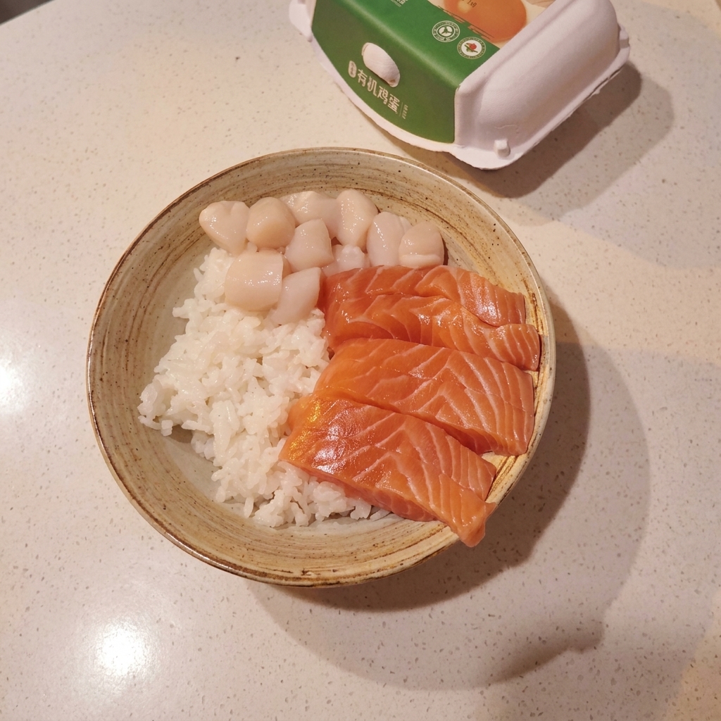 A bowl filled with a base of white sushi rice, topped with a neat arrangement of fresh salmon slices, scallops, and raw sweet shrimp.