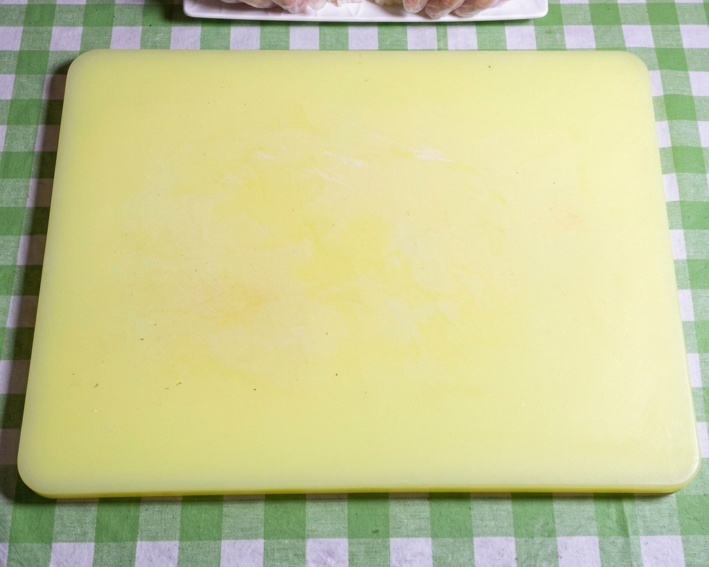 A close-up of gloved hands shaping sticky sushi rice into neat, uniform oval balls on a yellow cutting board.