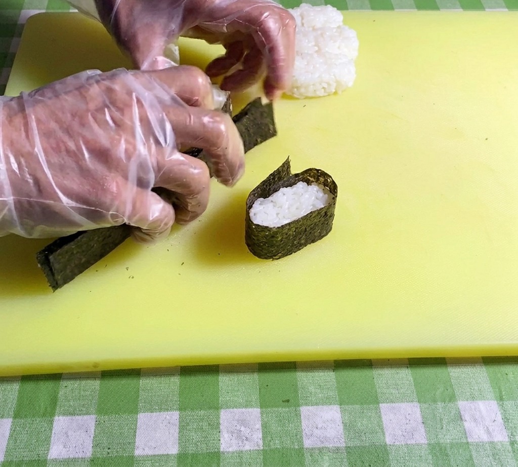 Close-up view of hands pressing the ends of a nori strip together to secure it around a rice base.