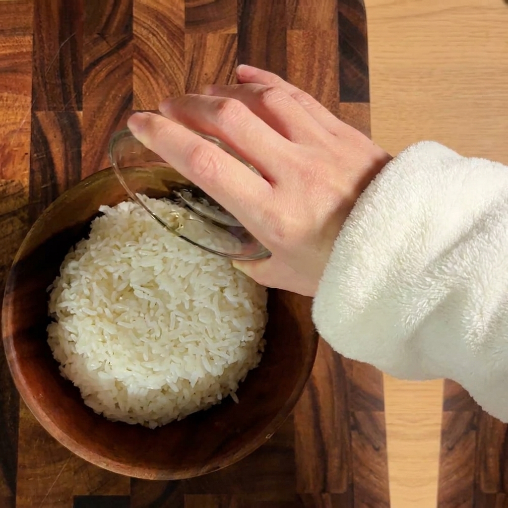 Cooked white rice being seasoned with sushi vinegar in a wooden bowl.