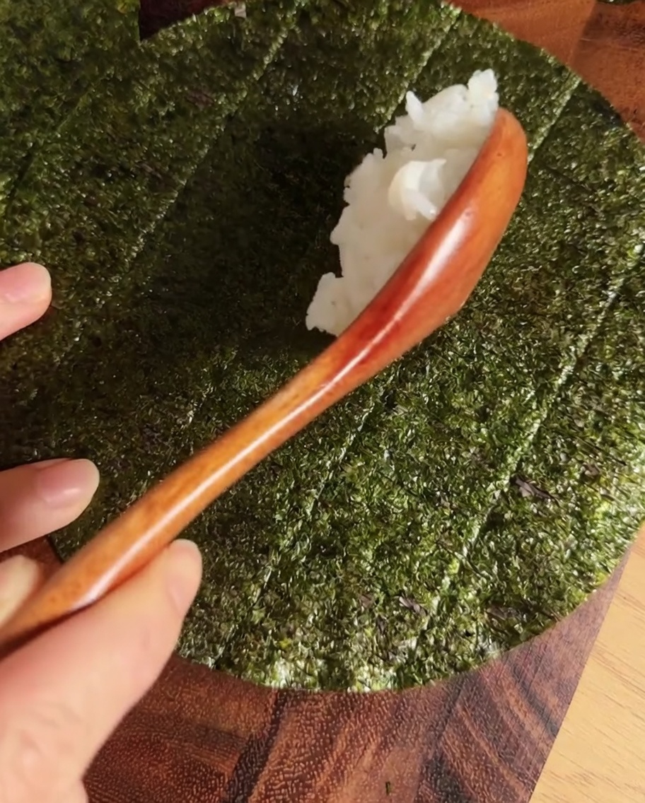 A stripe of seasoned sushi rice centered on a circular nori sheet.