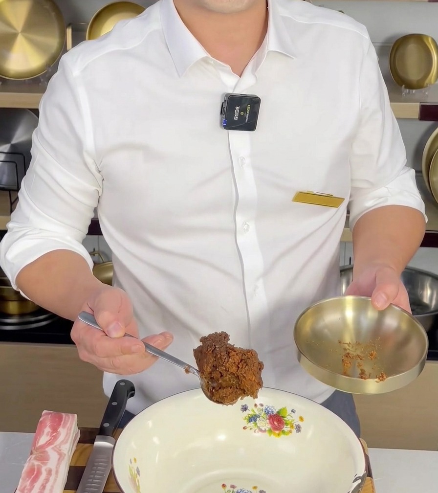 A spoonful of Doenjang being added to a white mixing bowl, ready to be mixed with other ingredients.