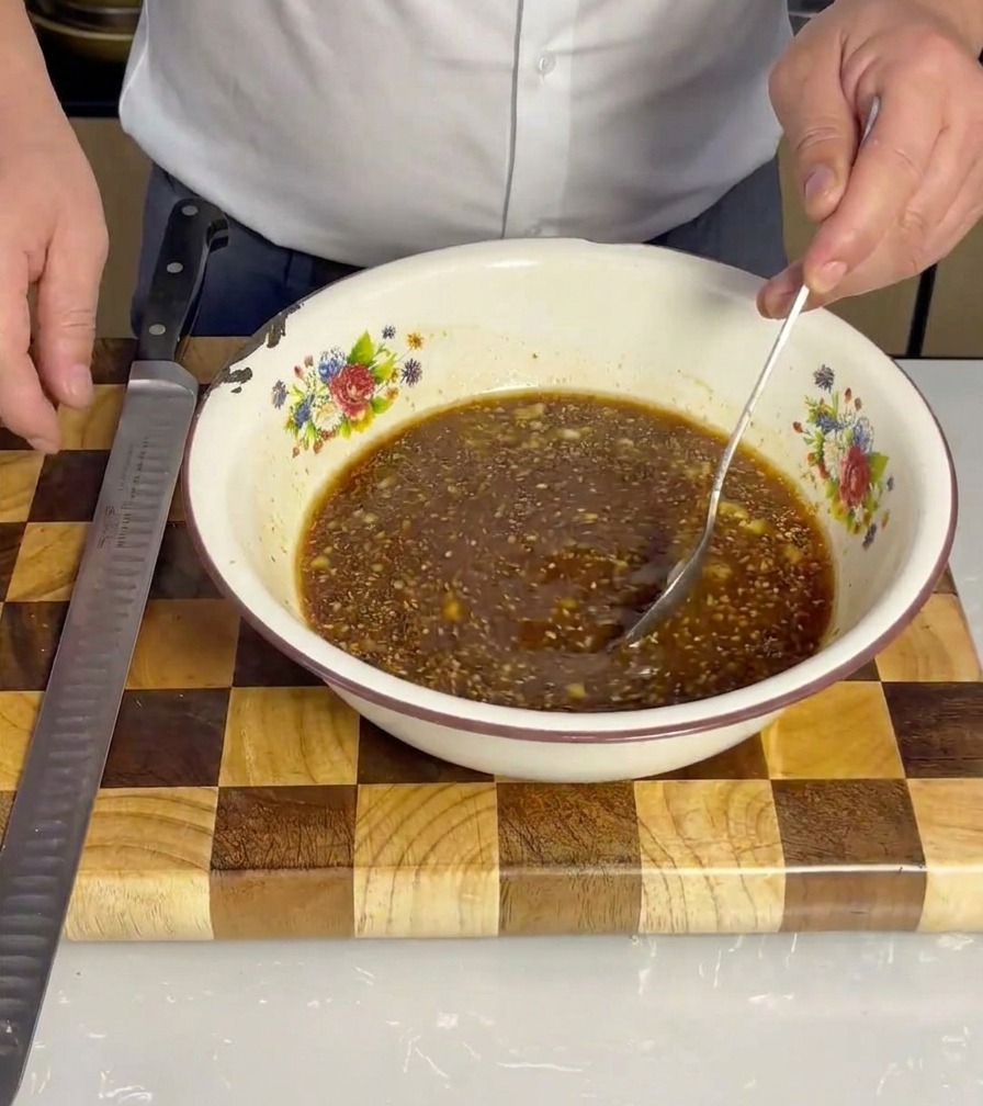 Sliced pork belly being placed into the marinade bowl, ensuring even coverage.