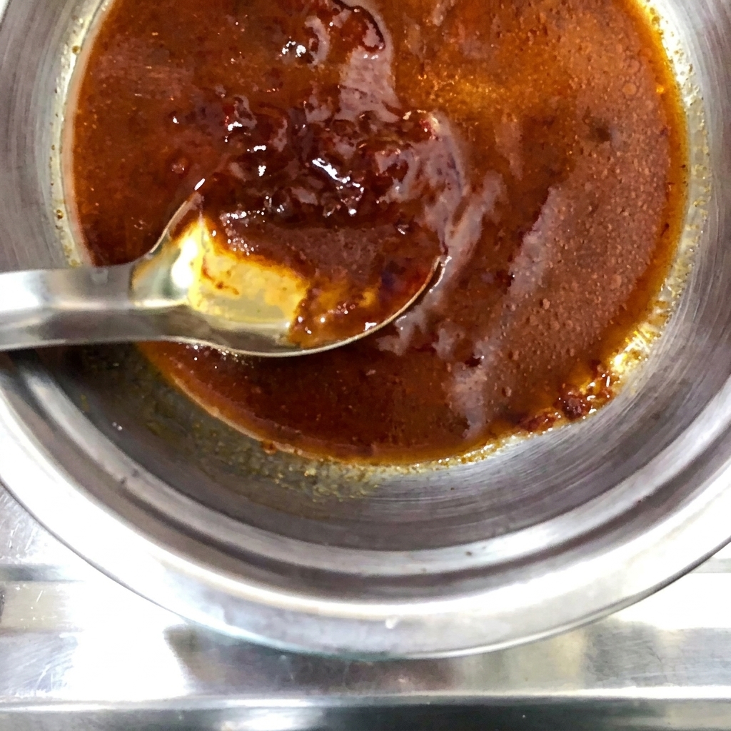 A dry spice powder being sprinkled over the prepared sauce mixture in the metal bowl.