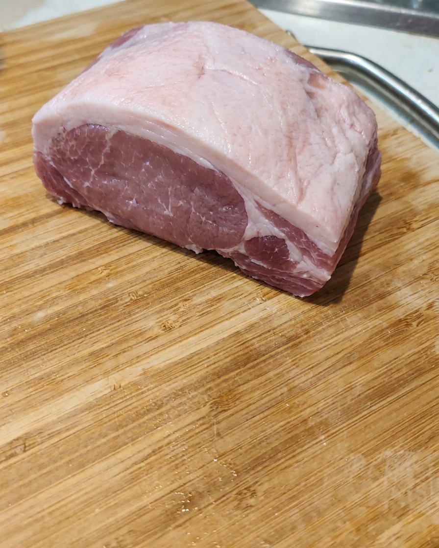 A close-up of a raw pork belly slab being sliced into thick, even portions on a wooden board.