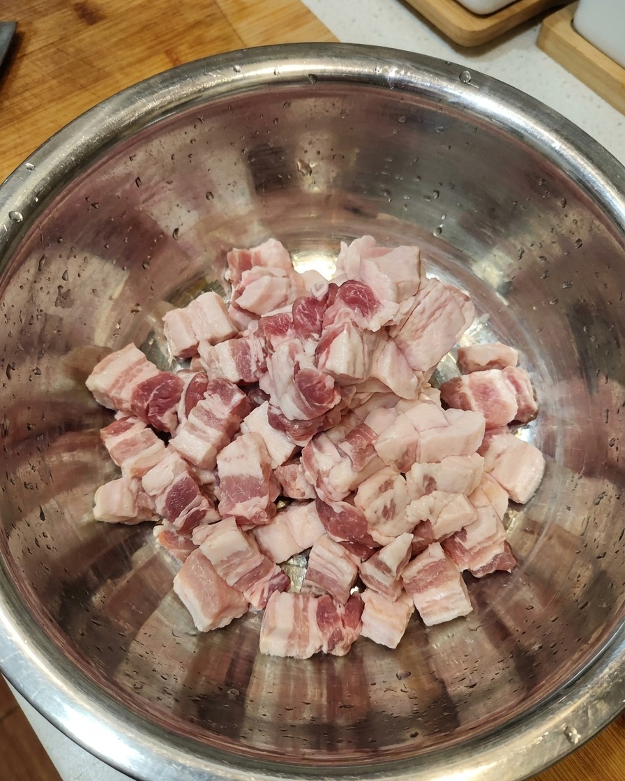 Slices of raw pork belly gathered together in a large stainless steel bowl.