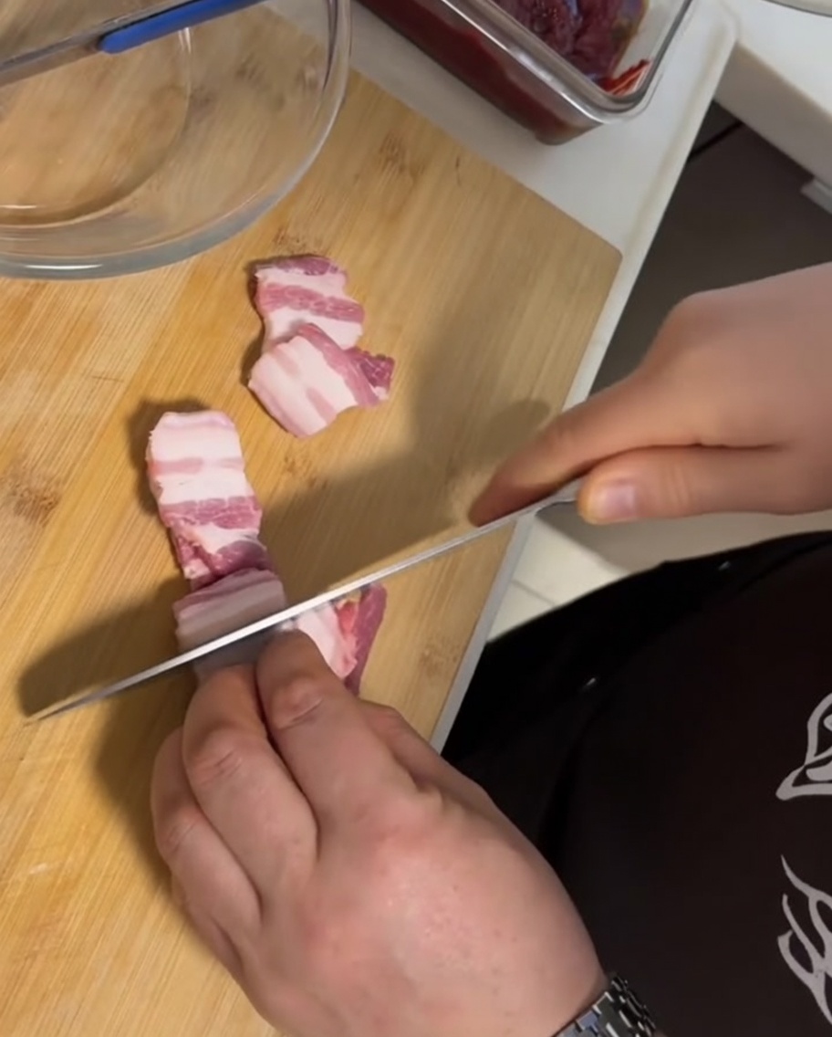 Thick slices of fresh, skin-on raw pork belly arranged on a wooden cutting board next to a knife.