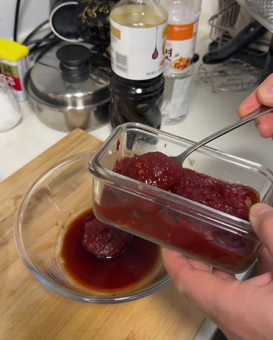 A thick, dark red sauce being mixed with a spoon in a clear glass bowl on a wooden surface.