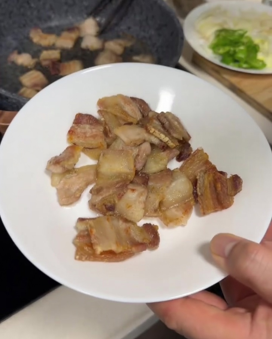 Pork belly slices frying in a grey pan, showing a golden-brown, slightly crispy exterior.