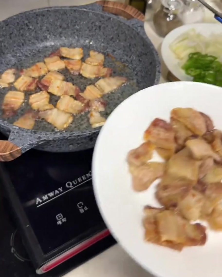Metal tongs placing browned, crispy pork belly slices onto a white plate.