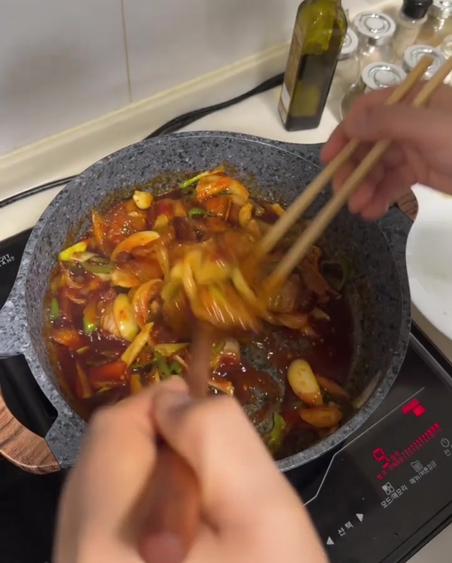 Pork belly and vegetable stir-fry being tossed in a red sauce in a pan.
