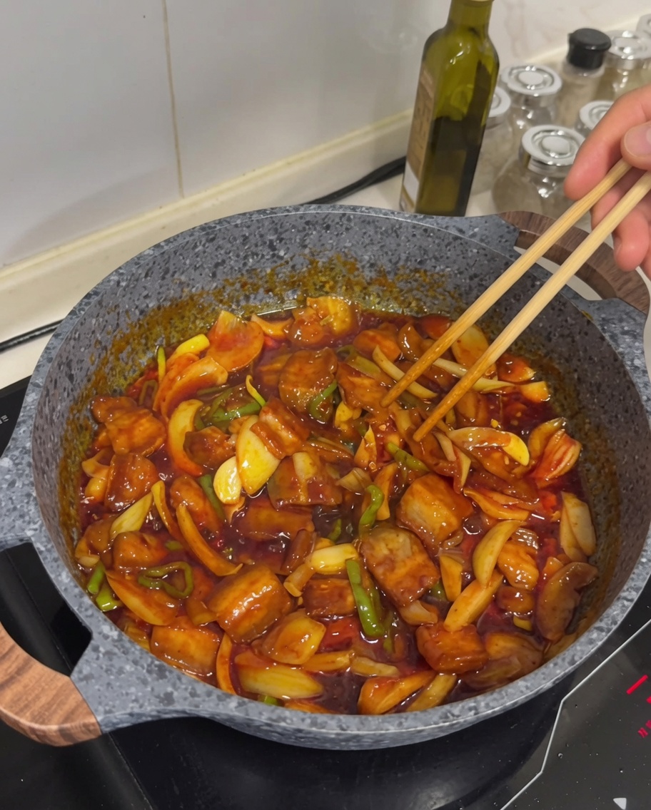 Finished spicy stir-fried pork belly in a pan topped with sesame seeds.