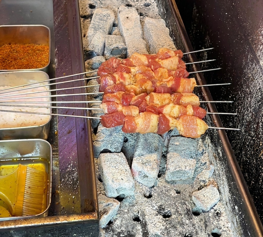 Raw pork belly skewers arranged on a hot charcoal grill, ready to begin cooking.