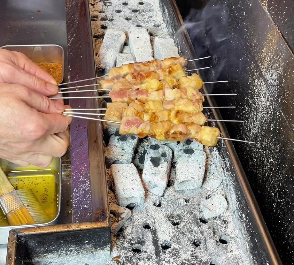 Chefs hands carefully manipulating the skewers to ensure even fat distribution across the cooking meat.