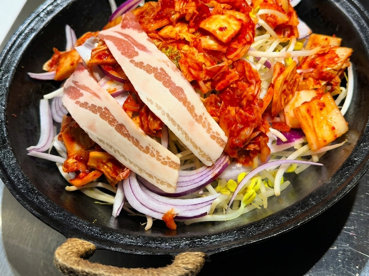 Slices of raw pork belly arranged carefully on top of a bed of kimchi, onions, and bean sprouts.