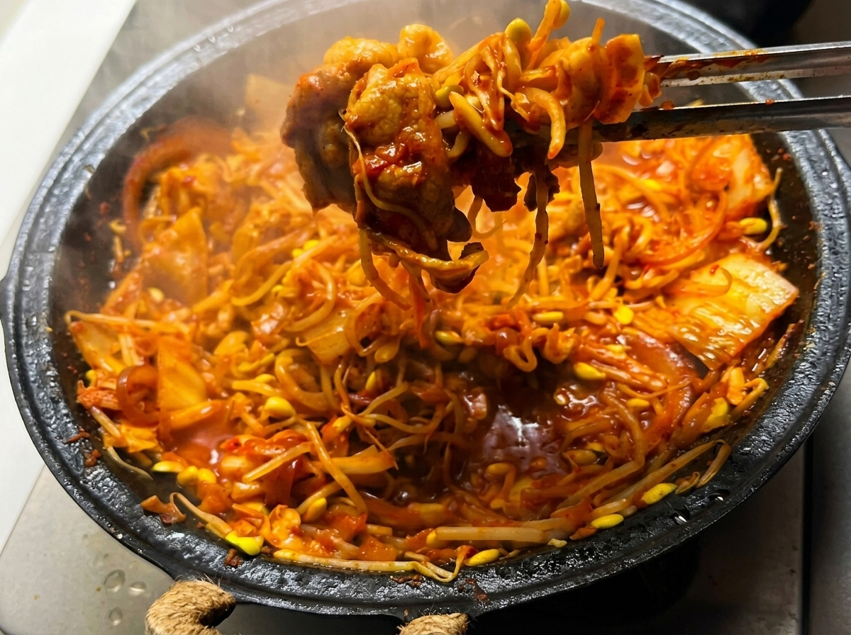 The Kimchi Pork Belly with Bean Sprouts mixture being stirred in the pan over a high flame.