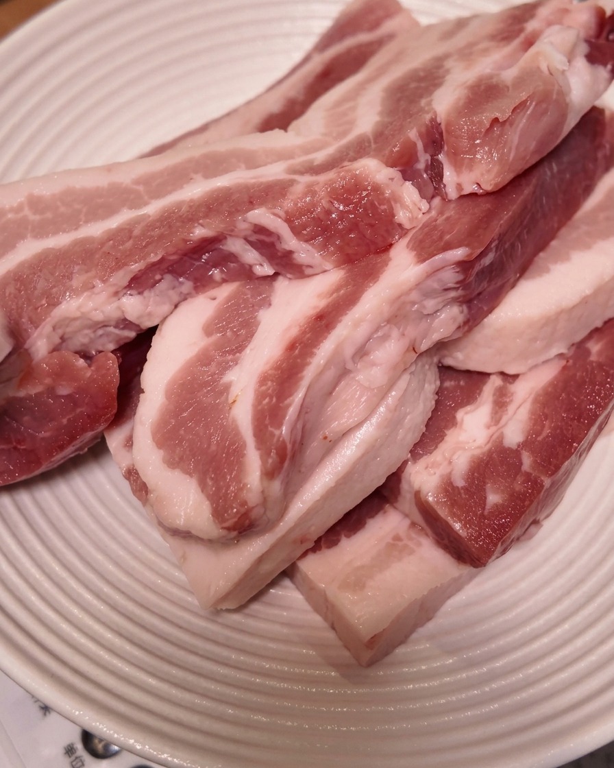 Thick slices of raw pork belly stacked on a white ridged plate.