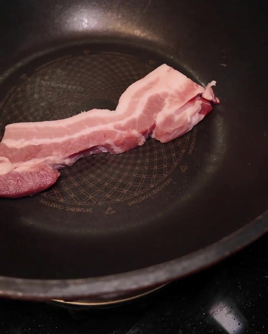 A thick slice of raw pork belly placed in a large black pan.