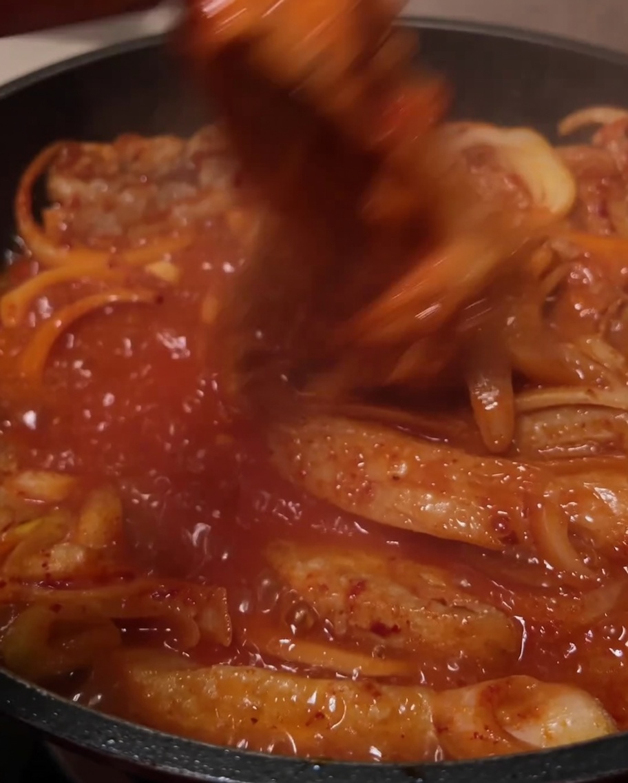 The ingredients being stirred together in the bubbling red sauce in the pan.