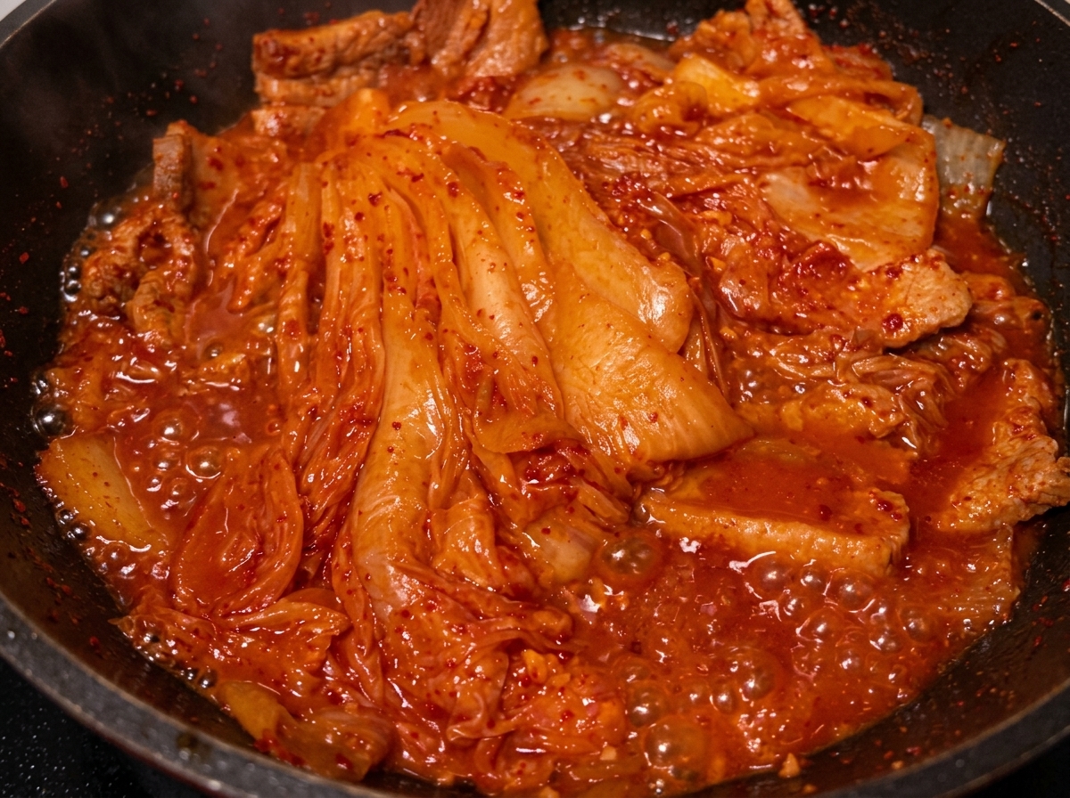 Oil being poured from a spoon into the pan with braised pork and kimchi.