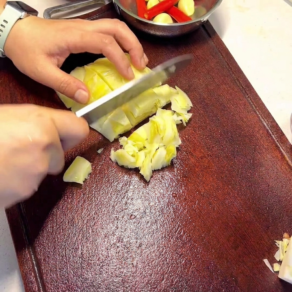 Hands holding a knife and slicing pieces of pale green pickled cabbage on a dark wooden cutting board.