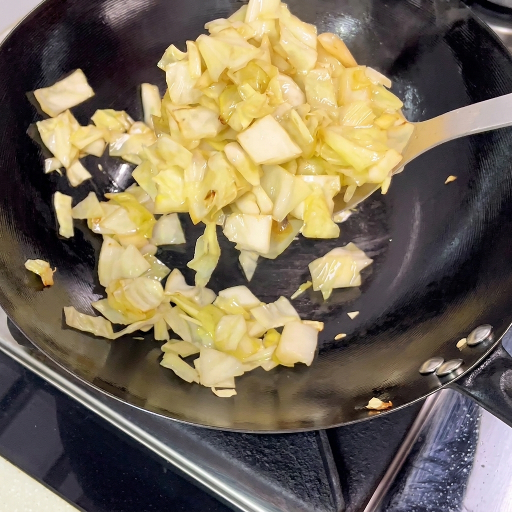 Pickled cabbage pieces being lifted out of a hot wok with a metal spatula.