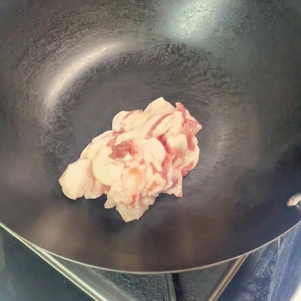 A heap of raw, sliced pork belly pieces placed in the center of an empty, preheated wok.