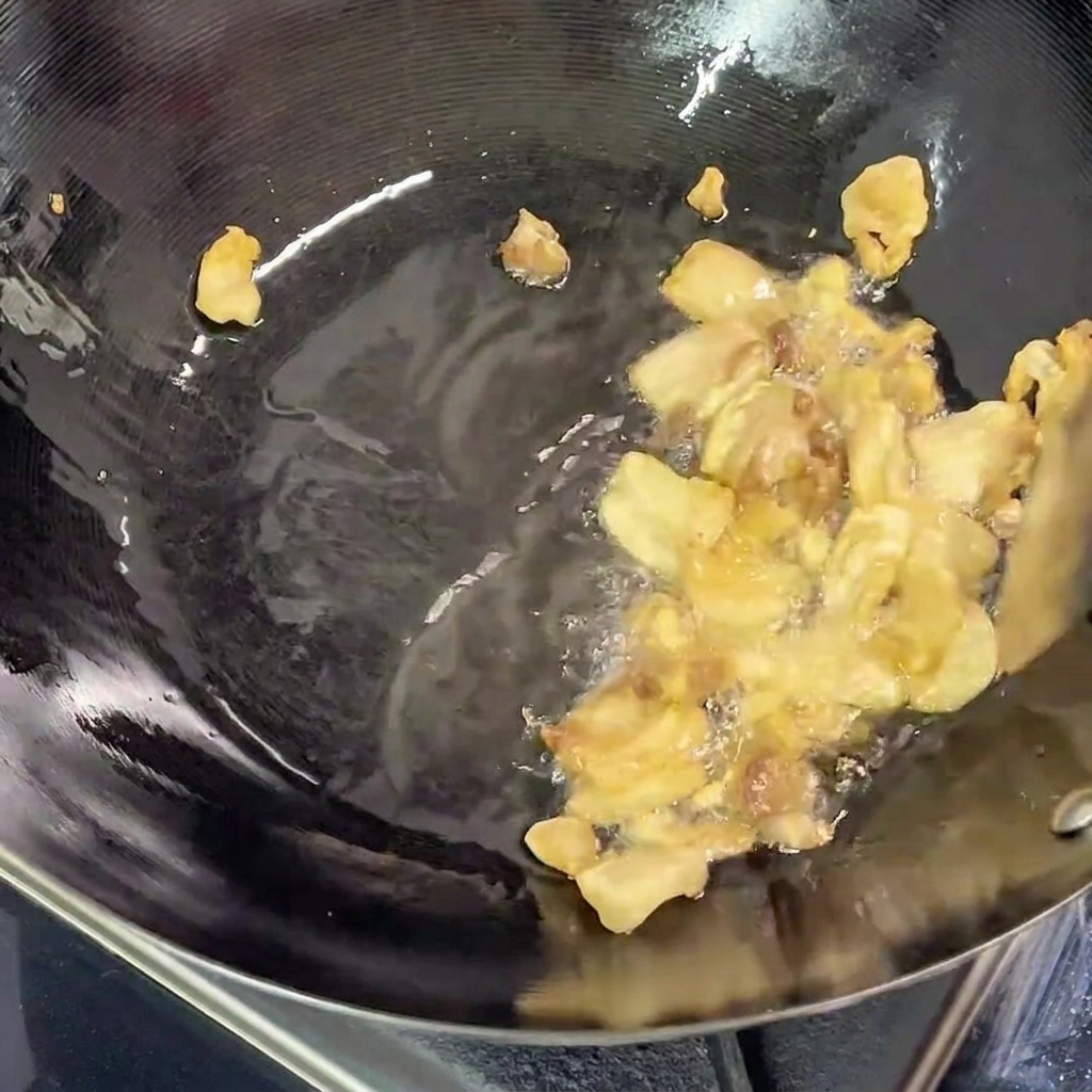 Pork belly pieces frying in the wok, with clear rendered fat visible at the bottom of the pan.