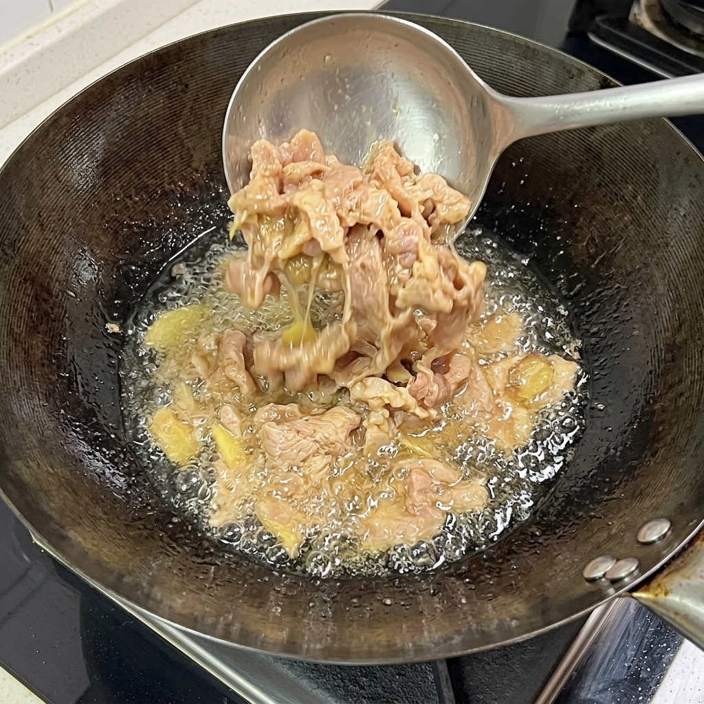 Slices of pork frying in the wok, showing a cooked, browned exterior surface.