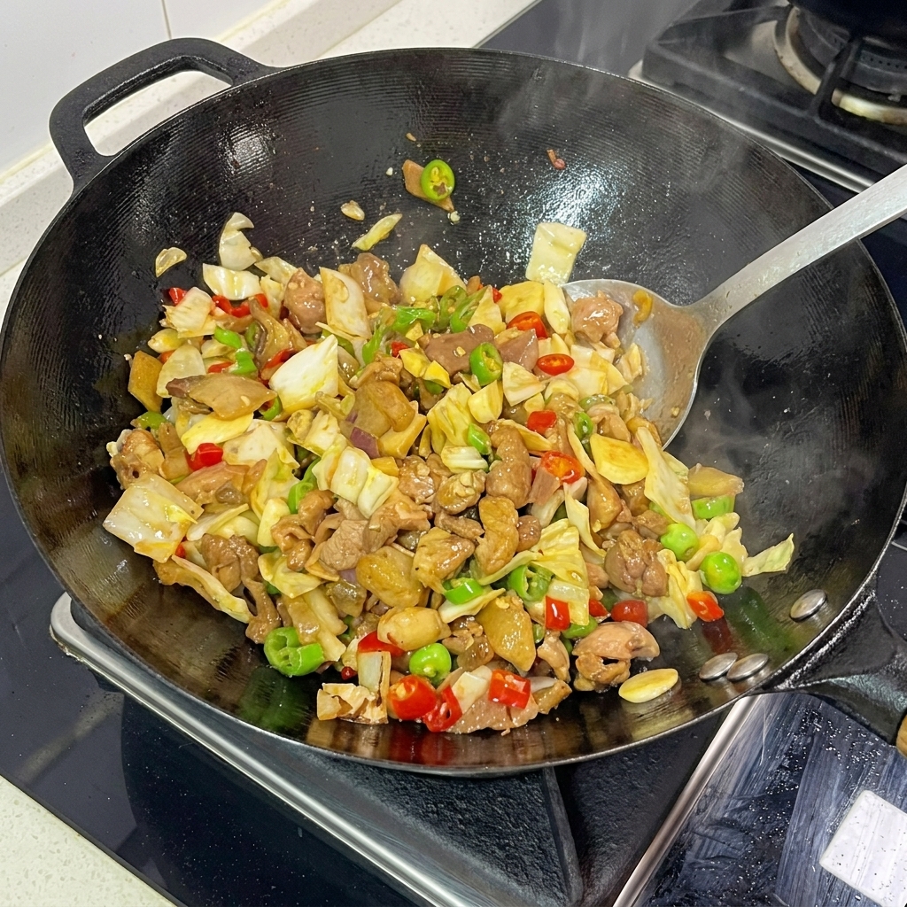 A metal spatula actively tossing pickled cabbage, sliced pork, and chopped chilies together in a steaming hot wok.