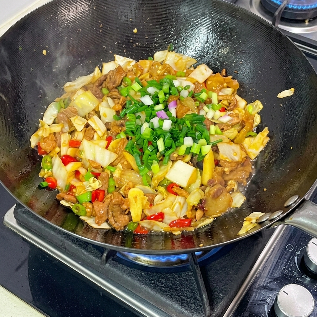 Bright green chopped scallions sprinkled heavily over the finished pickled cabbage and pork stir-fry in the wok.