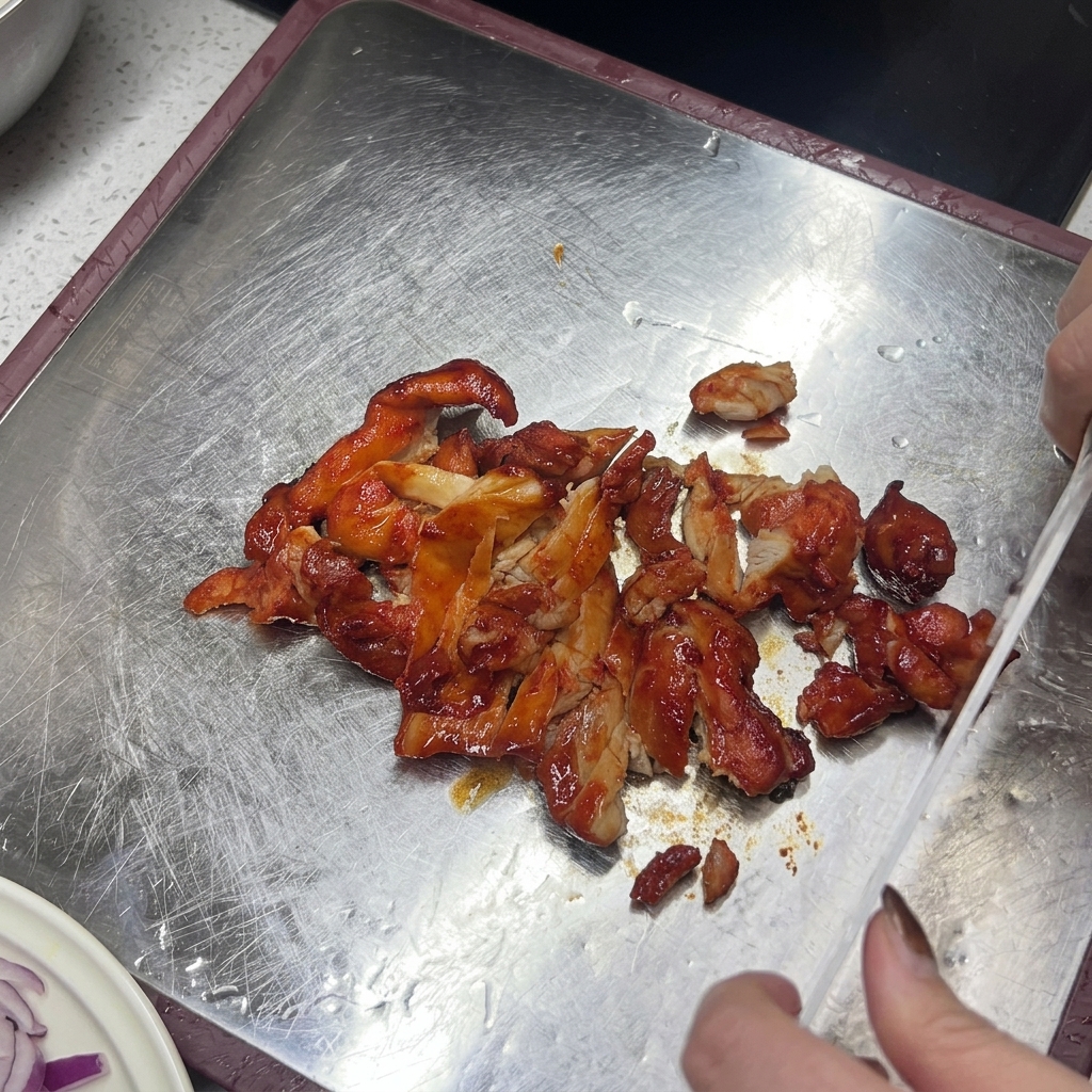 A knife slicing through cooked, reddish-brown glazed chicken on a metallic cutting board.
