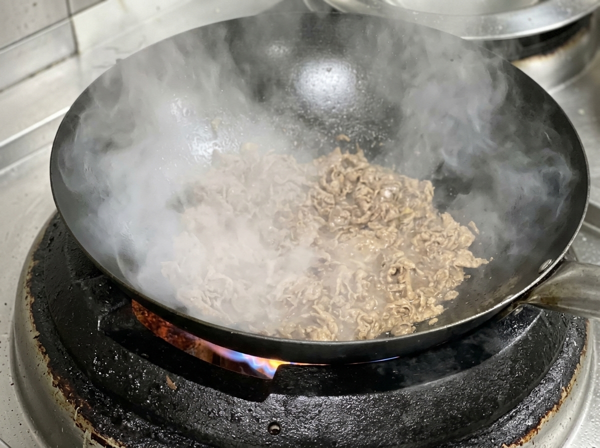 Slices of beef and onion cooking together in a hot, seasoned wok.