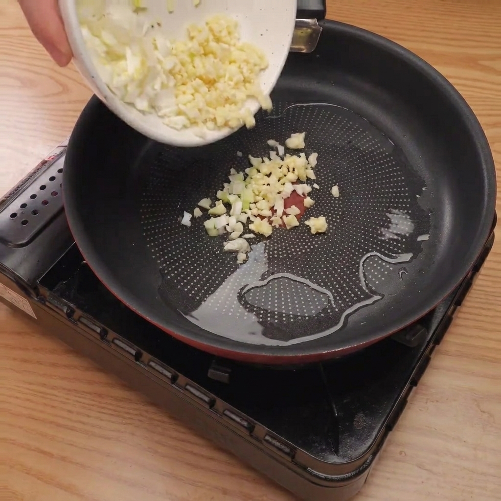 Finely diced onion, green onion, and garlic sizzling in a hot pan with oil.