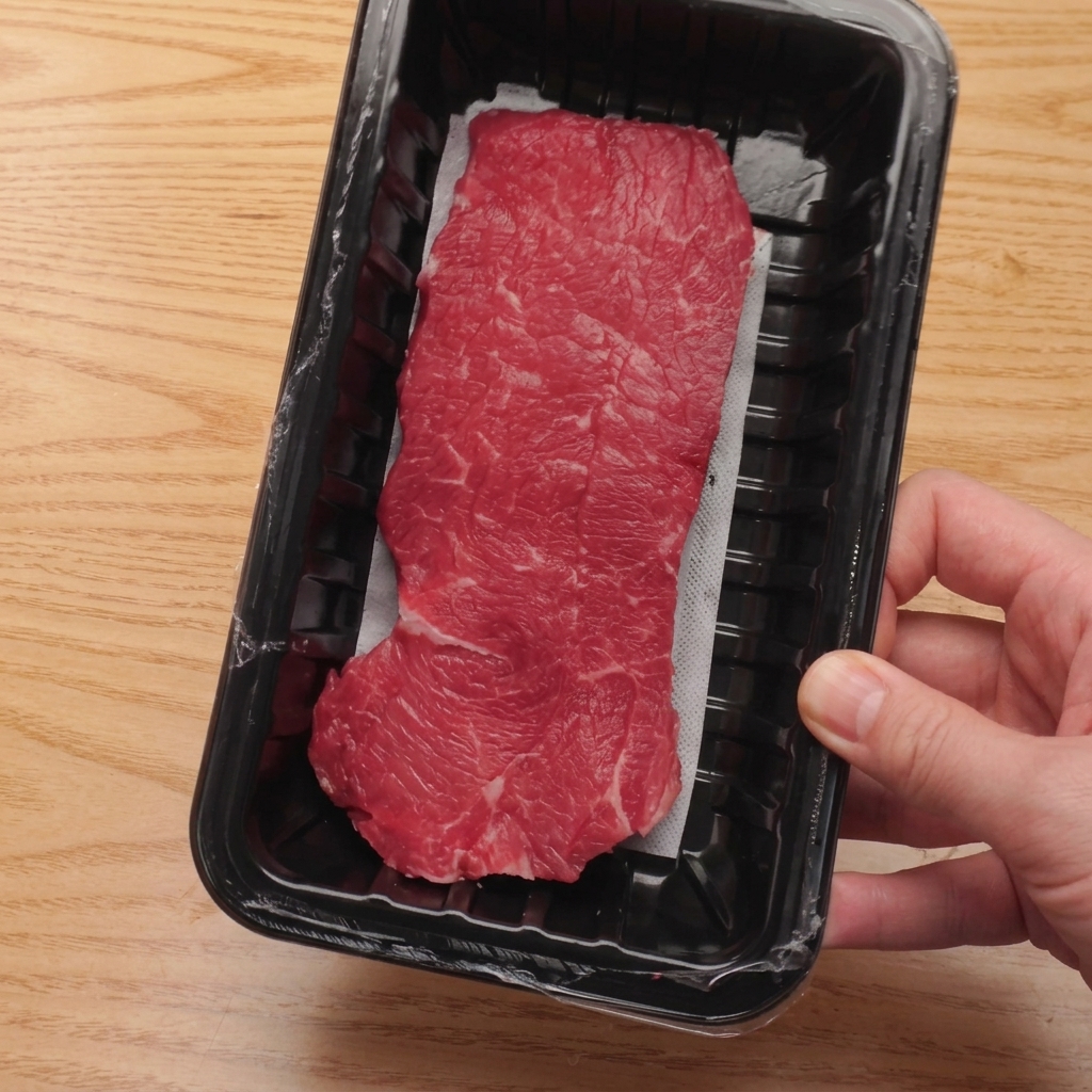 Raw beef tenderloin being sliced into consistent cubes on a wooden cutting board.