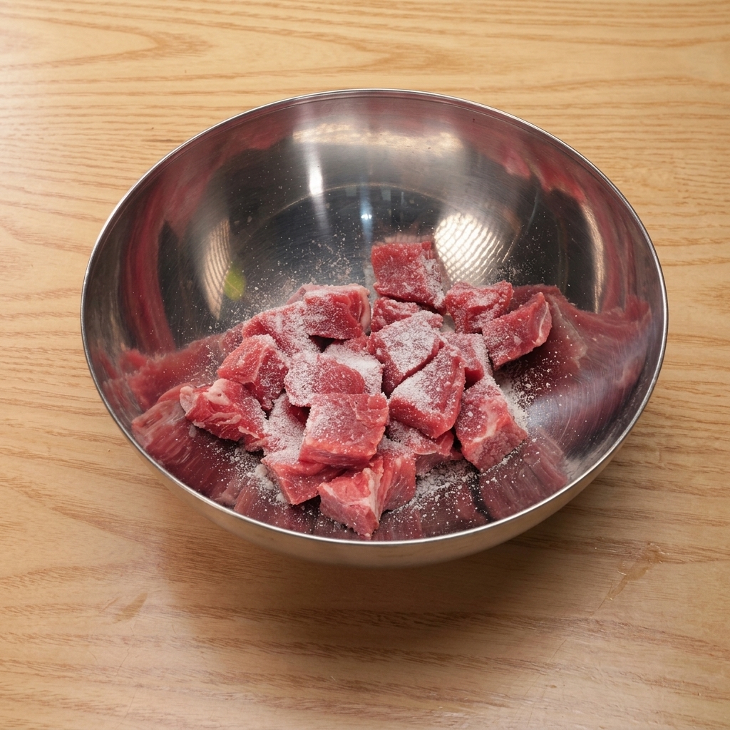 Cubed beef in a metal mixing bowl being coated with salt, sugar, soy sauce, and starch.