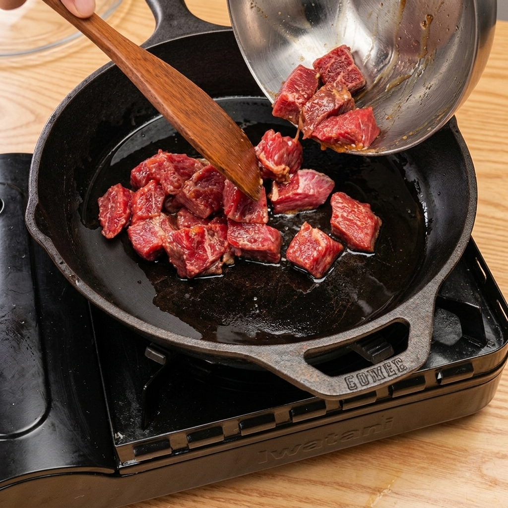 Beef cubes browning in a cast-iron skillet, with steam rising after adding cooking wine and covering.
