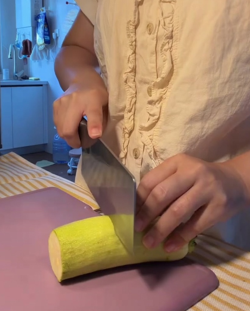 Fresh zucchini being sliced into neat semi-circular pieces on a purple cutting board.